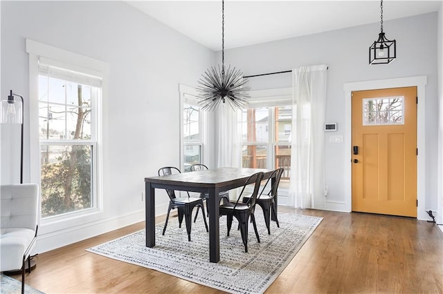 dining area with a chandelier, wood finished floors, healthy amount of natural light, and baseboards