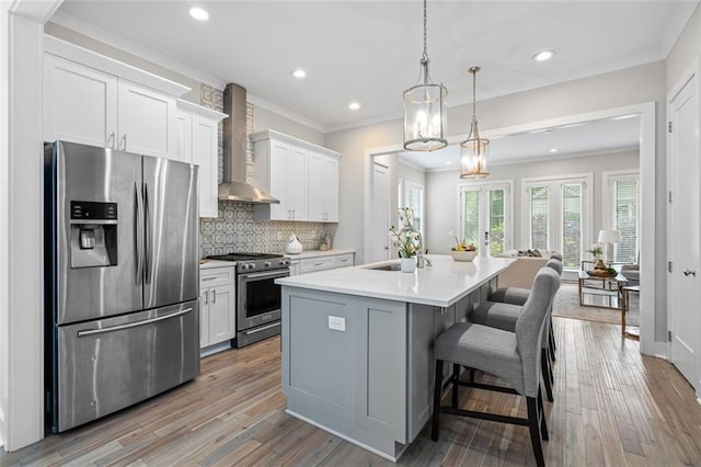 kitchen with stainless steel appliances, wall chimney exhaust hood, a sink, ornamental molding, and a center island with sink