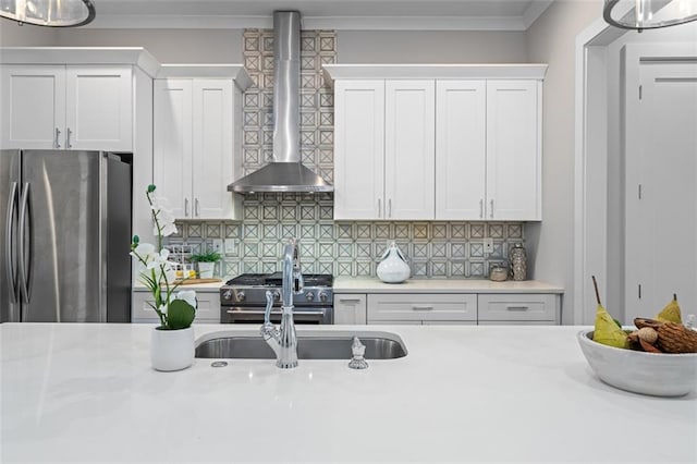 kitchen featuring stainless steel appliances, wall chimney exhaust hood, light countertops, white cabinetry, and crown molding