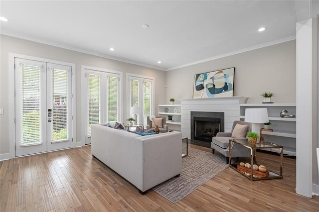 living room with crown molding, a fireplace with flush hearth, wood finished floors, recessed lighting, and french doors