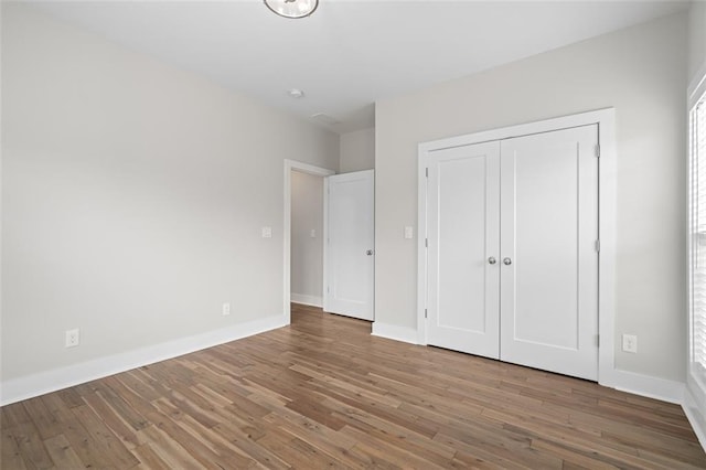 unfurnished bedroom featuring wood finished floors, baseboards, and a closet