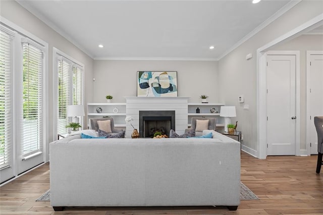 living area featuring plenty of natural light, crown molding, a fireplace, light wood finished floors, and recessed lighting