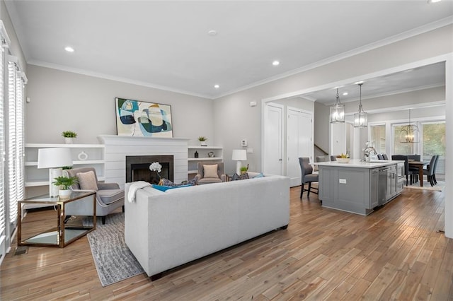 living room with light wood-type flooring, recessed lighting, a fireplace, a chandelier, and crown molding