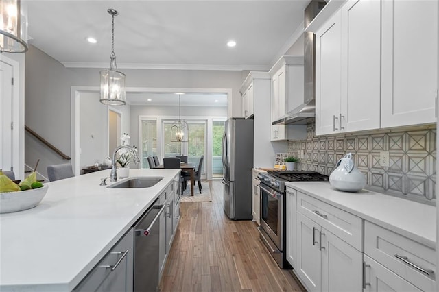 kitchen featuring appliances with stainless steel finishes, wall chimney exhaust hood, a sink, white cabinetry, and recessed lighting
