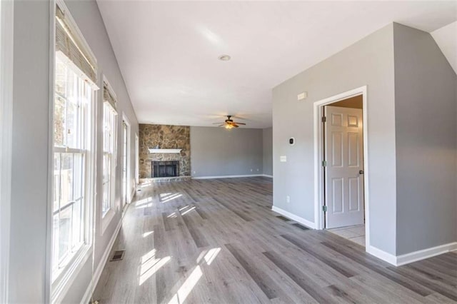 unfurnished living room with light hardwood / wood-style floors, a stone fireplace, and ceiling fan