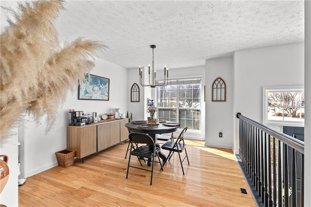 dining area with an inviting chandelier, a textured ceiling, and light wood-type flooring