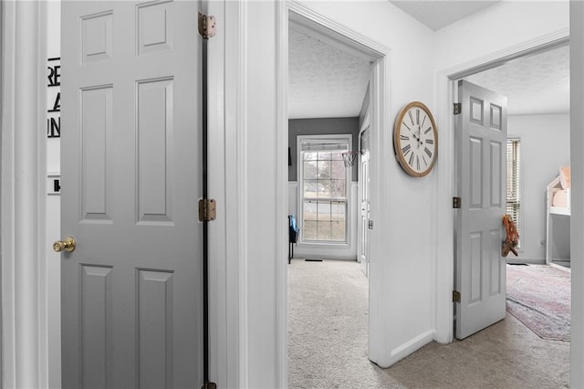 hallway with light colored carpet and a textured ceiling