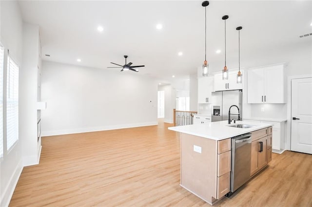 kitchen with light wood-style flooring, appliances with stainless steel finishes, a kitchen island with sink, light countertops, and a sink