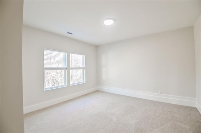 spare room featuring light colored carpet, visible vents, and baseboards