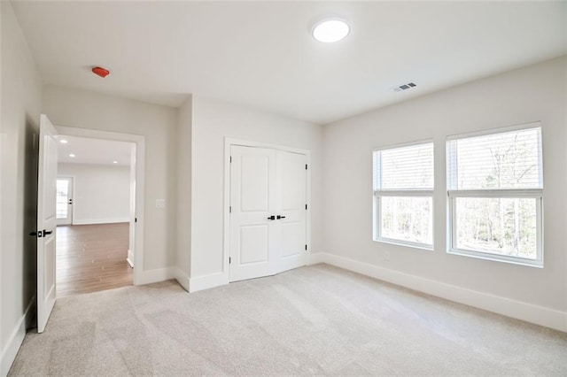 unfurnished bedroom featuring visible vents, baseboards, a closet, and light colored carpet