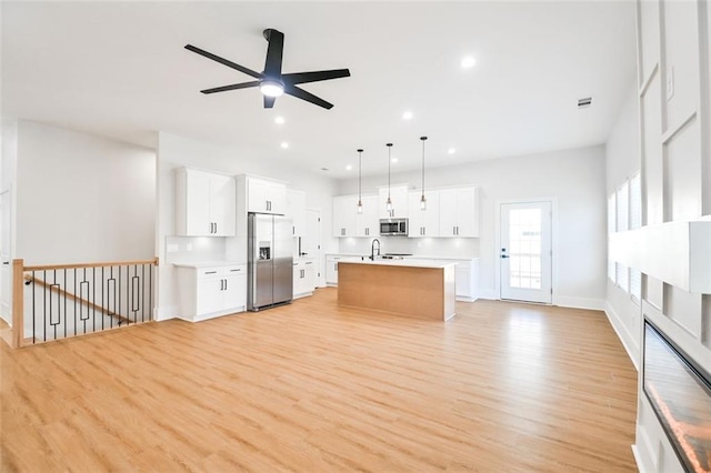 kitchen featuring light wood-style flooring, a center island with sink, stainless steel appliances, and light countertops