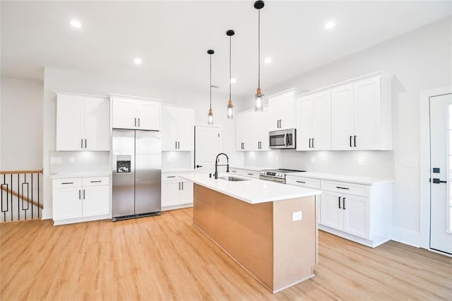 kitchen with a center island with sink, stainless steel appliances, light countertops, light wood-type flooring, and a sink