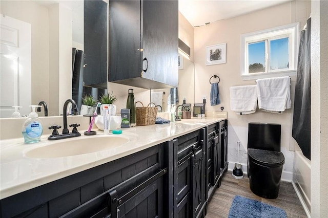 full bathroom with baseboards, double vanity, a sink, and wood finished floors