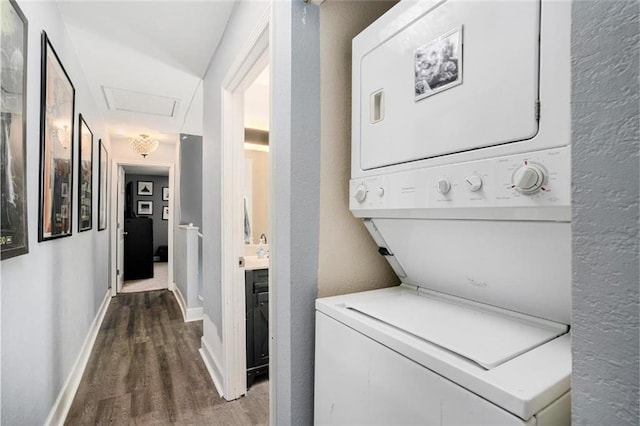 clothes washing area with attic access, wood finished floors, stacked washer / dryer, laundry area, and baseboards