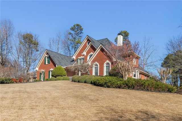 view of front of home with a front lawn, a chimney, and brick siding