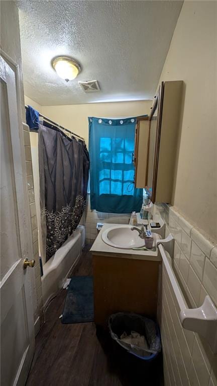 bathroom featuring a textured ceiling, hardwood / wood-style flooring, shower / bathtub combination with curtain, tile walls, and vanity