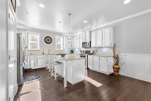 kitchen with a kitchen island, a sink, appliances with stainless steel finishes, dark wood-style floors, and crown molding