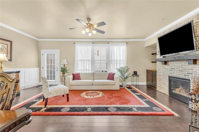 living room with ornamental molding, a brick fireplace, wainscoting, and wood finished floors