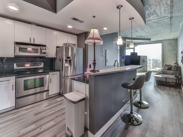 361 17th St NW Unit 1121, Atlanta, GA 30363 - kitchen featuring decorative light fixtures, white cabinets, light wood-type flooring, a kitchen island, and stainless steel appliances