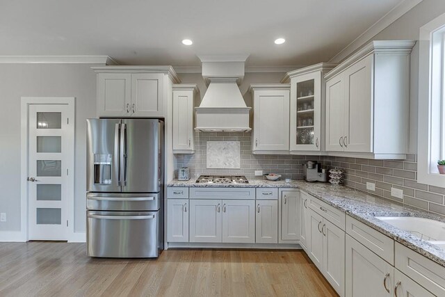 3441 Shoreland Dr, Buford, GA 30518 - kitchen featuring appliances with stainless steel finishes, premium range hood, crown molding, decorative backsplash, and light wood finished floors