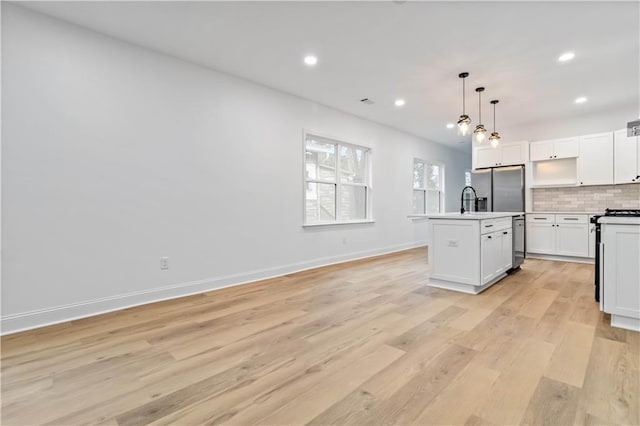 kitchen with stainless steel appliances, backsplash, pendant lighting, light hardwood / wood-style floors, and a kitchen island with sink