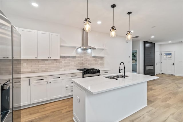 kitchen with gas range, white cabinetry, sink, decorative light fixtures, and a kitchen island with sink