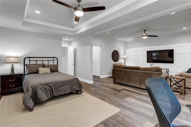 bedroom with ceiling fan, light hardwood / wood-style floors, and a raised ceiling