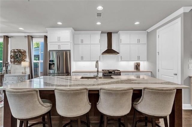 kitchen with a kitchen island with sink, white cabinets, stainless steel appliances, and wall chimney range hood