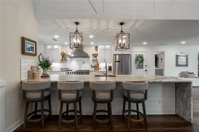 kitchen with wall chimney range hood, open shelves, a notable chandelier, a sink, and high end appliances