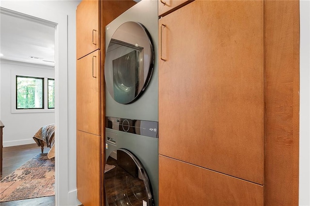 clothes washing area featuring stacked washer and dryer, dark hardwood / wood-style flooring, and cabinets