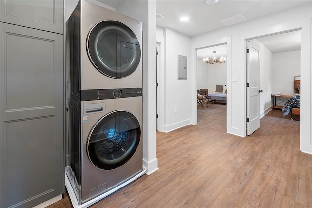 clothes washing area with an inviting chandelier, hardwood / wood-style flooring, stacked washer / dryer, and electric panel