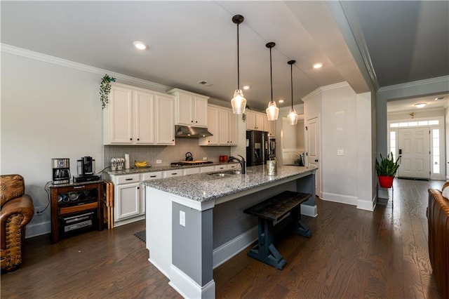 kitchen featuring under cabinet range hood, a sink, black fridge with ice dispenser, stainless steel gas cooktop, and baseboards