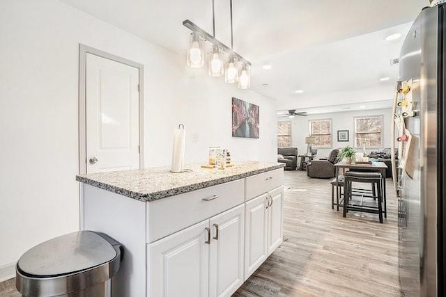 kitchen featuring pendant lighting, light wood finished floors, freestanding refrigerator, open floor plan, and white cabinets