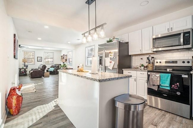 kitchen with stainless steel appliances, a center island, white cabinets, open floor plan, and decorative backsplash