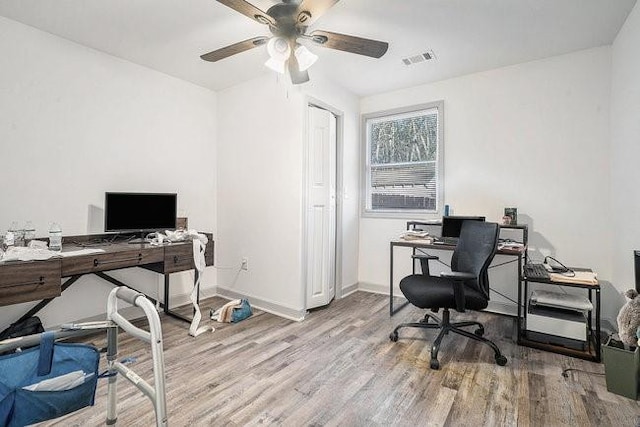 office space featuring light wood-style floors, baseboards, visible vents, and a ceiling fan