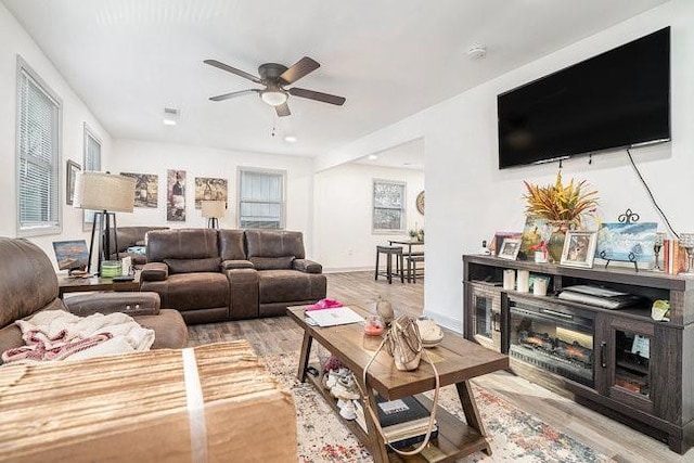 living area featuring ceiling fan, baseboards, wood finished floors, and a glass covered fireplace