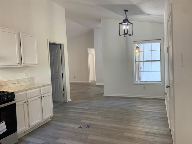 kitchen featuring white cabinetry, pendant lighting, vaulted ceiling, and range