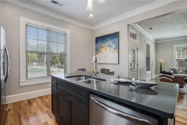 kitchen with sink, light hardwood / wood-style flooring, crown molding, an island with sink, and appliances with stainless steel finishes