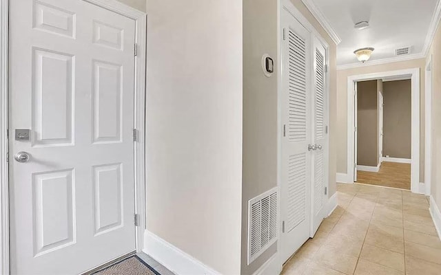 hall with light tile patterned flooring, baseboards, visible vents, and ornamental molding