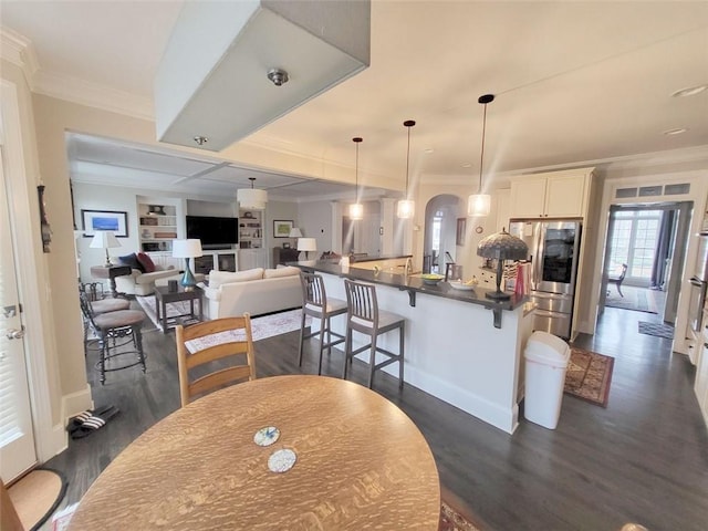 dining room featuring dark wood-type flooring, built in shelves, arched walkways, and ornamental molding