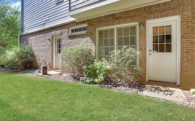 view of exterior entry featuring brick siding and a lawn