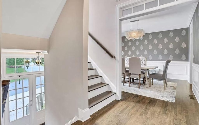 stairway featuring wallpapered walls, a notable chandelier, wood finished floors, and wainscoting