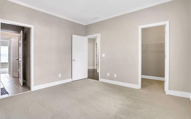 unfurnished bedroom with a spacious closet, carpet flooring, crown molding, and baseboards