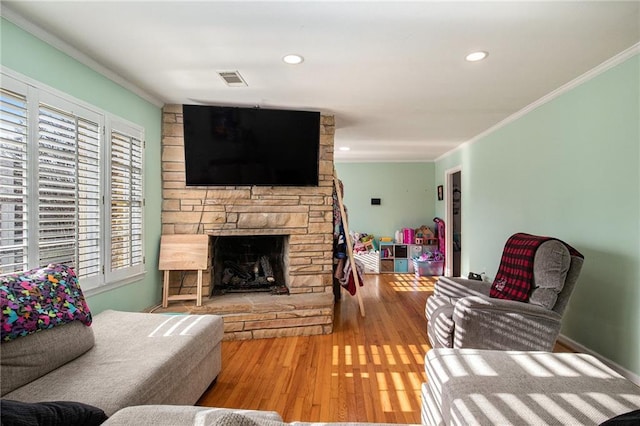 living area featuring a stone fireplace, recessed lighting, crown molding, and wood finished floors