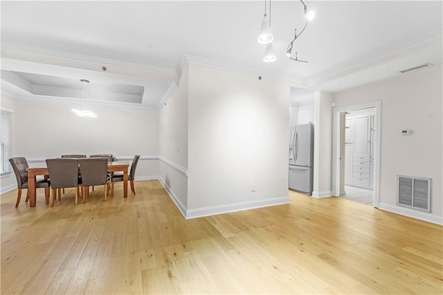 dining space featuring ornamental molding, a tray ceiling, and light hardwood / wood-style flooring