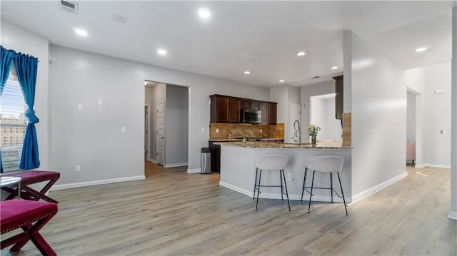 kitchen with sink, light hardwood / wood-style floors, light stone countertops, decorative backsplash, and kitchen peninsula