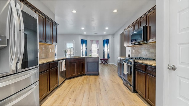 kitchen with sink, light hardwood / wood-style flooring, stainless steel appliances, light stone countertops, and backsplash