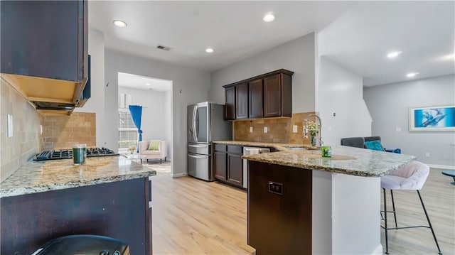 kitchen featuring sink, appliances with stainless steel finishes, a kitchen breakfast bar, kitchen peninsula, and light hardwood / wood-style floors