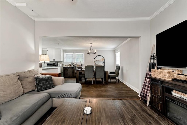 living area featuring dark wood-type flooring, a notable chandelier, crown molding, and baseboards