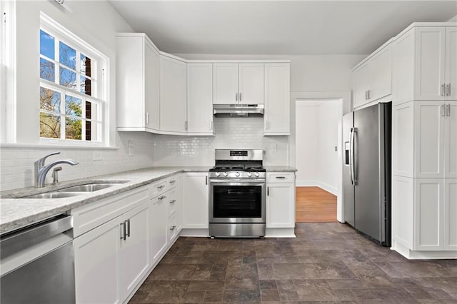 kitchen featuring under cabinet range hood, a sink, tasteful backsplash, appliances with stainless steel finishes, and white cabinets